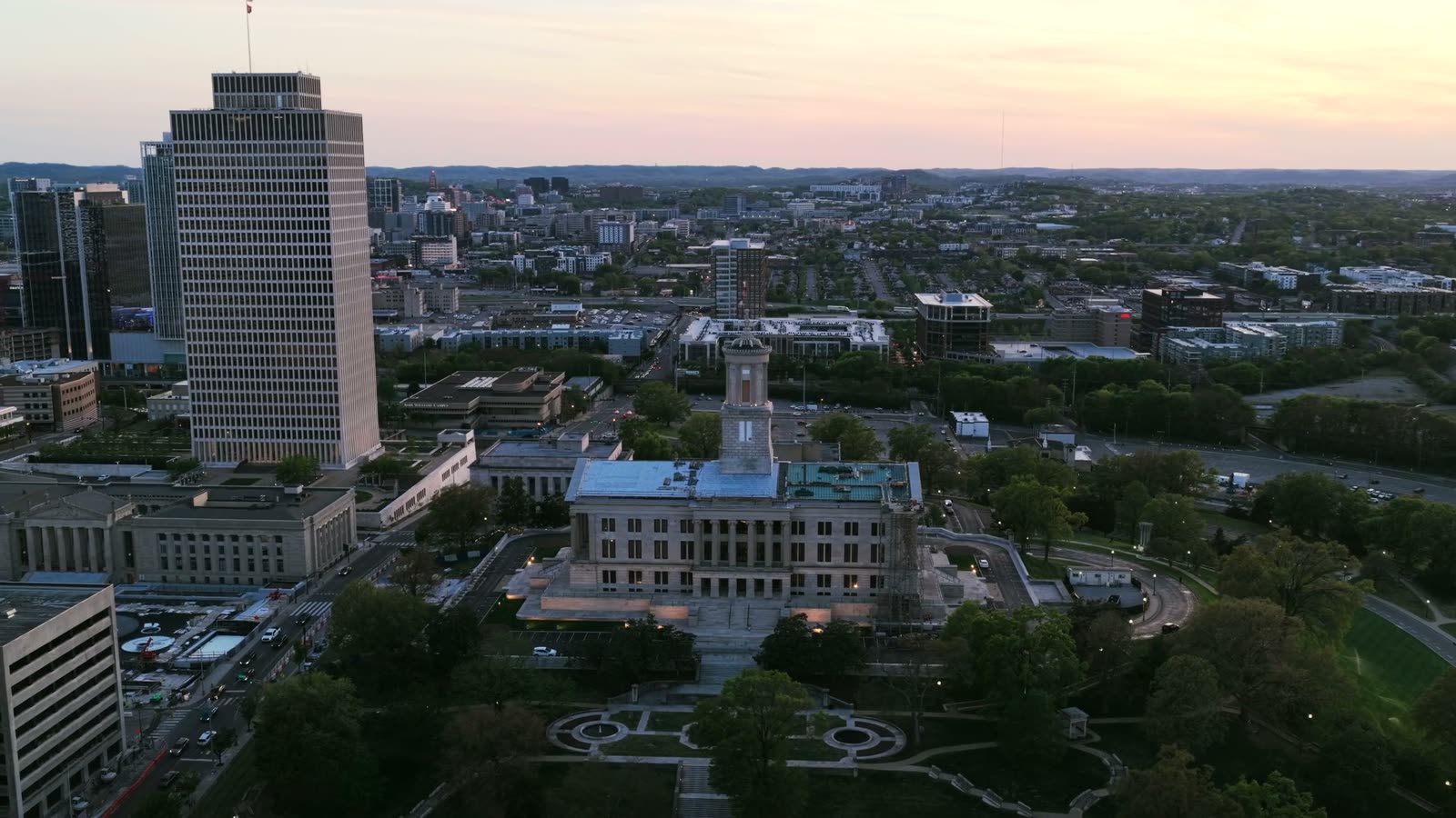 Golden hour aerial of a civic quarter, a stone administration building among office towers